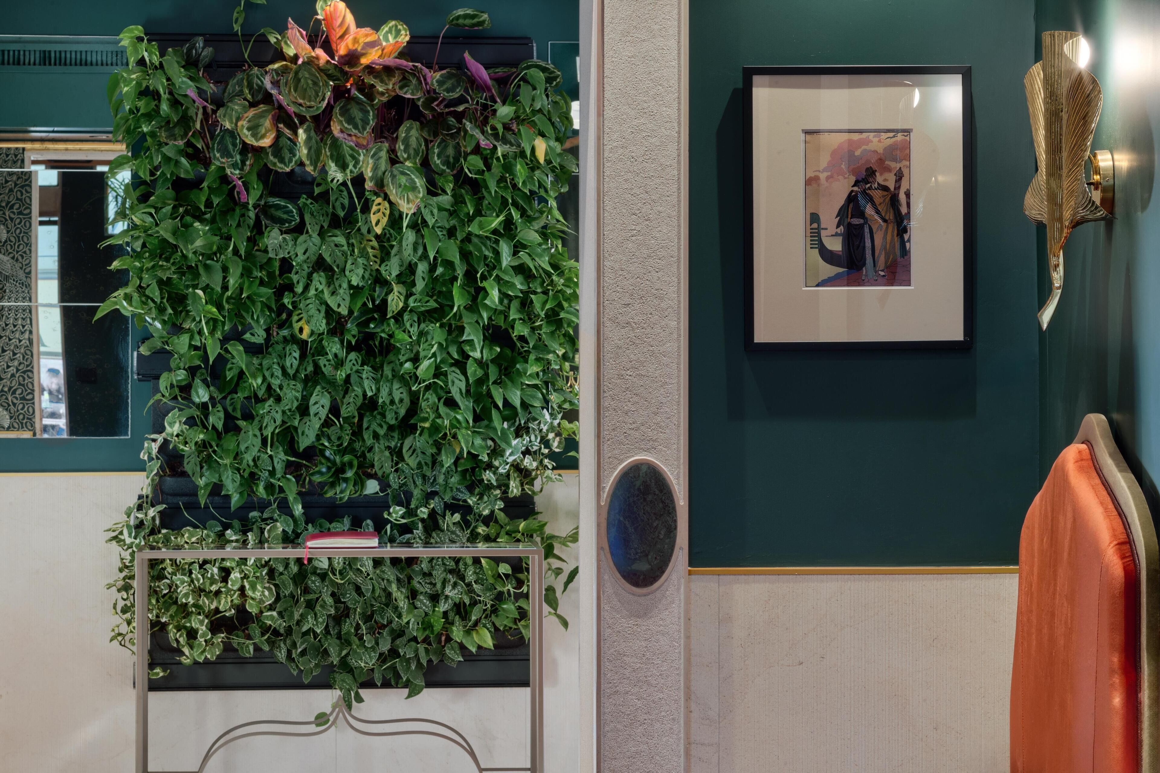 A room with a green wall, a framed picture, a decorative wall panel, and a plant wall.