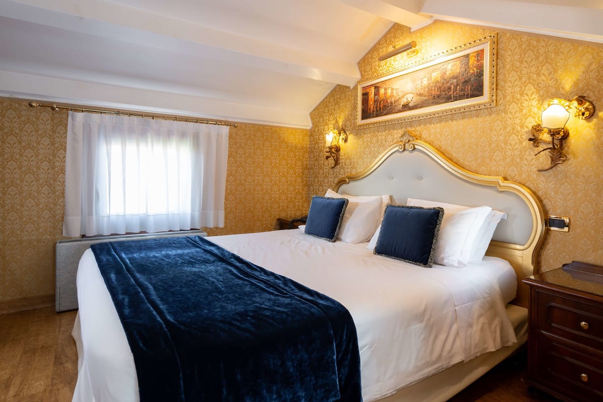 A hotel room with a large bed, a nightstand, a dresser, a painting on the wall, and a window with curtains.