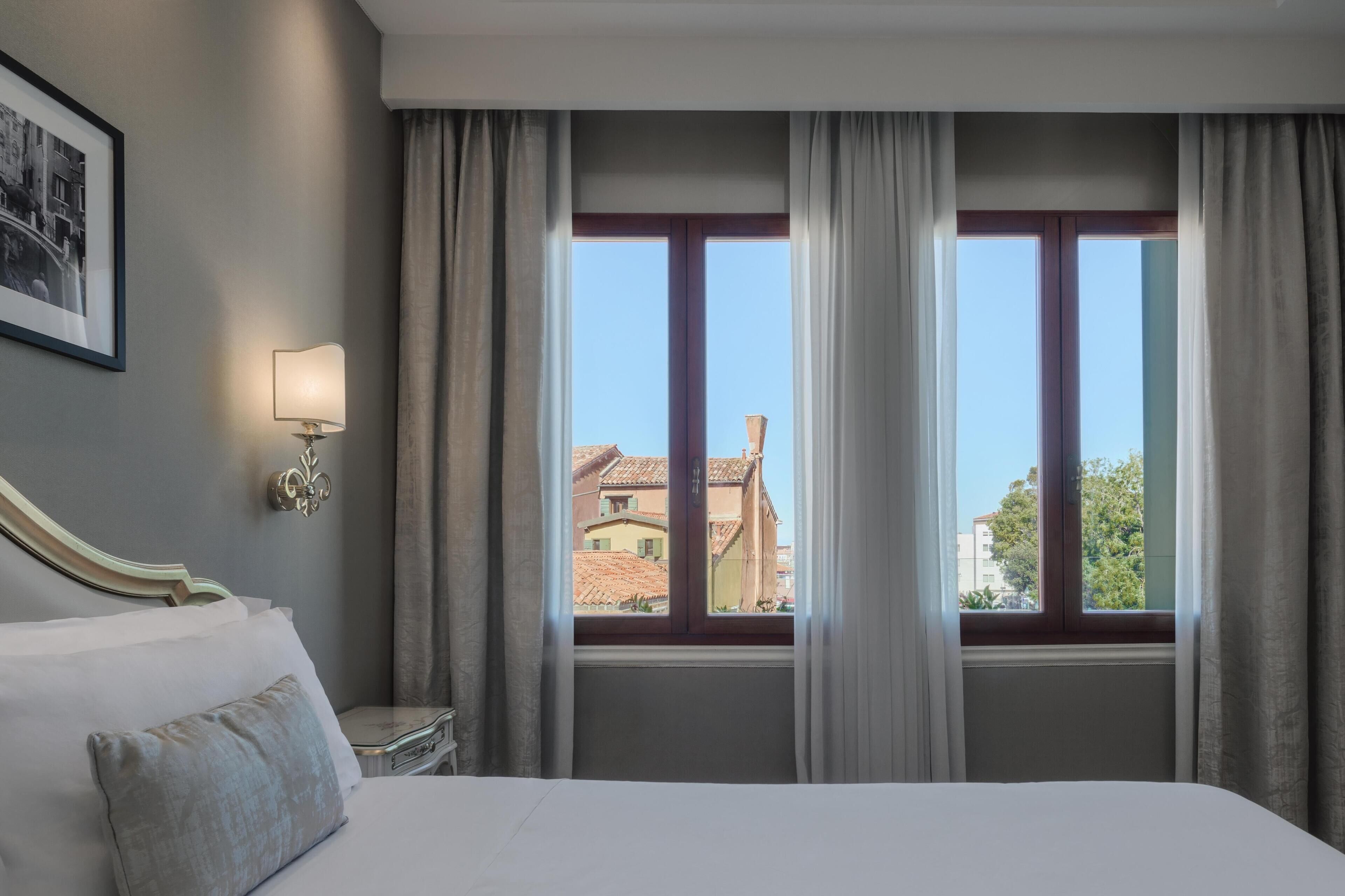 Una habitación de hotel con una cama grande, una mesita de noche con lámpara y una ventana con cortinas.