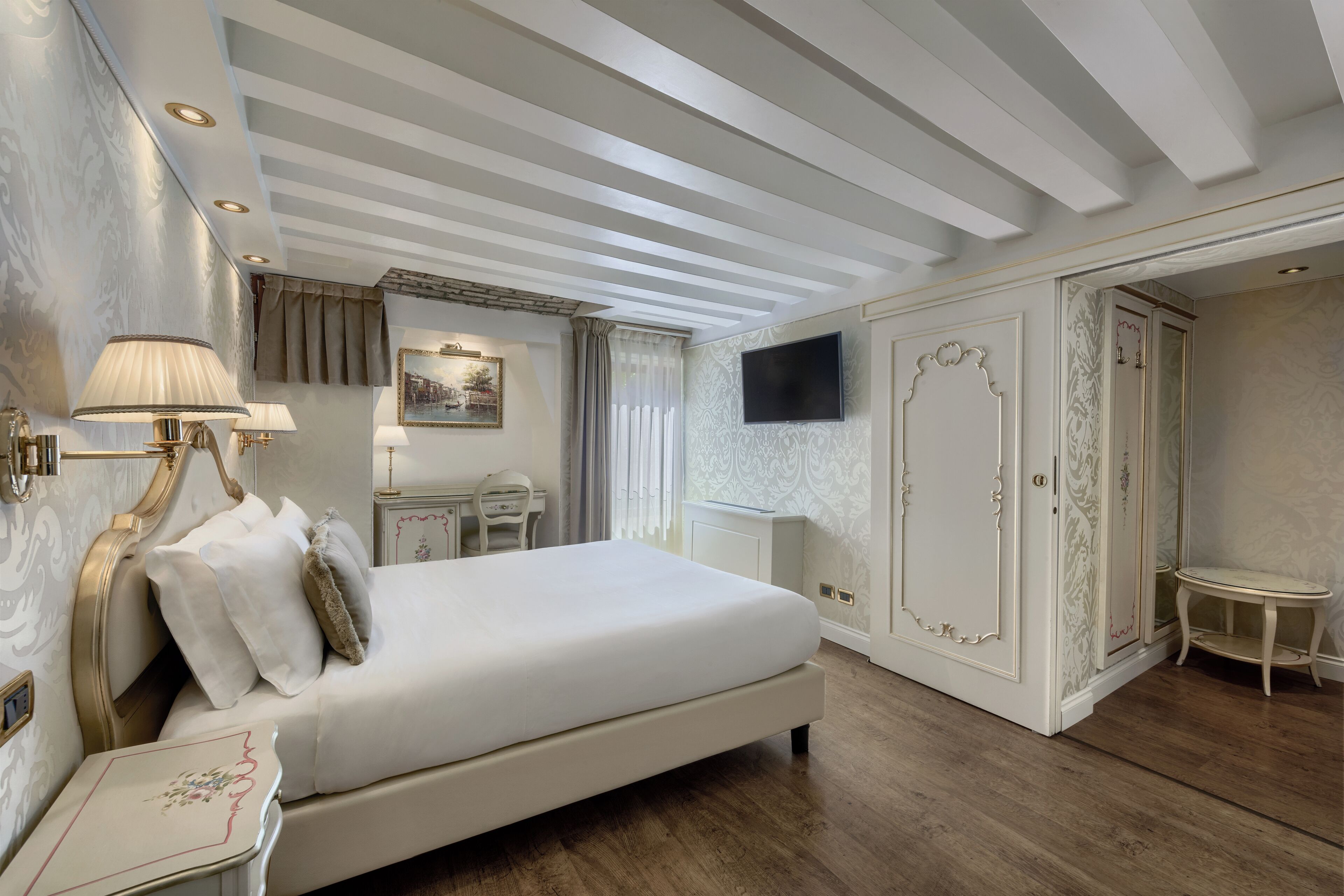 A spacious bedroom with a large bed, a desk, a television, and a wardrobe.