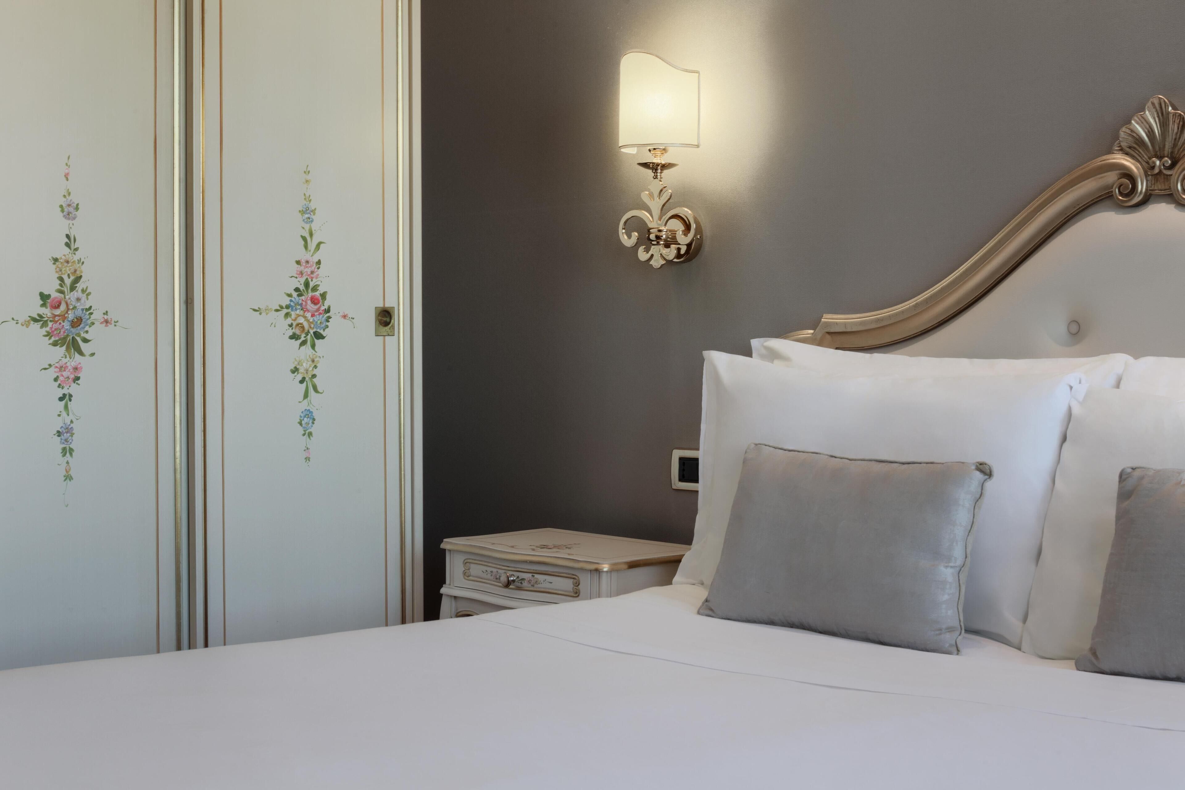 Una cama bien hecha con almohadas, una mesita de noche, una lámpara de pared y adornos florales en la pared.
