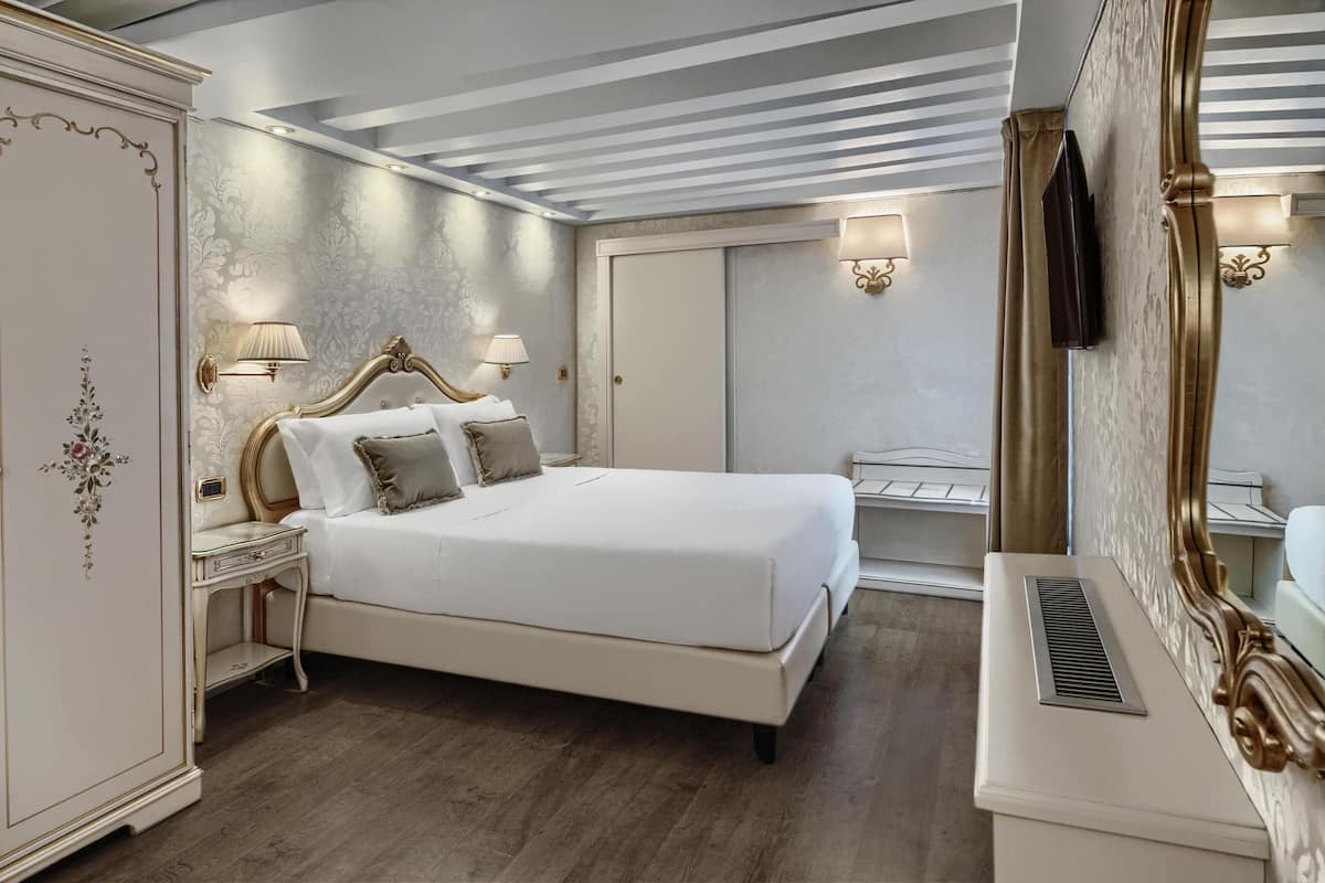 A bedroom with a large bed, bedside lamps, a wardrobe, and a television.