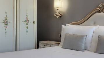 Una cama bien tendida con almohadas, una mesita de noche con lámpara y una pared decorada con motivos florales.