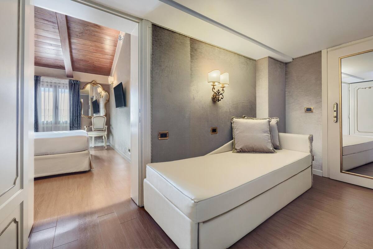 A modern bedroom with a large bed, a vanity with a mirror, and a wall-mounted light fixture.