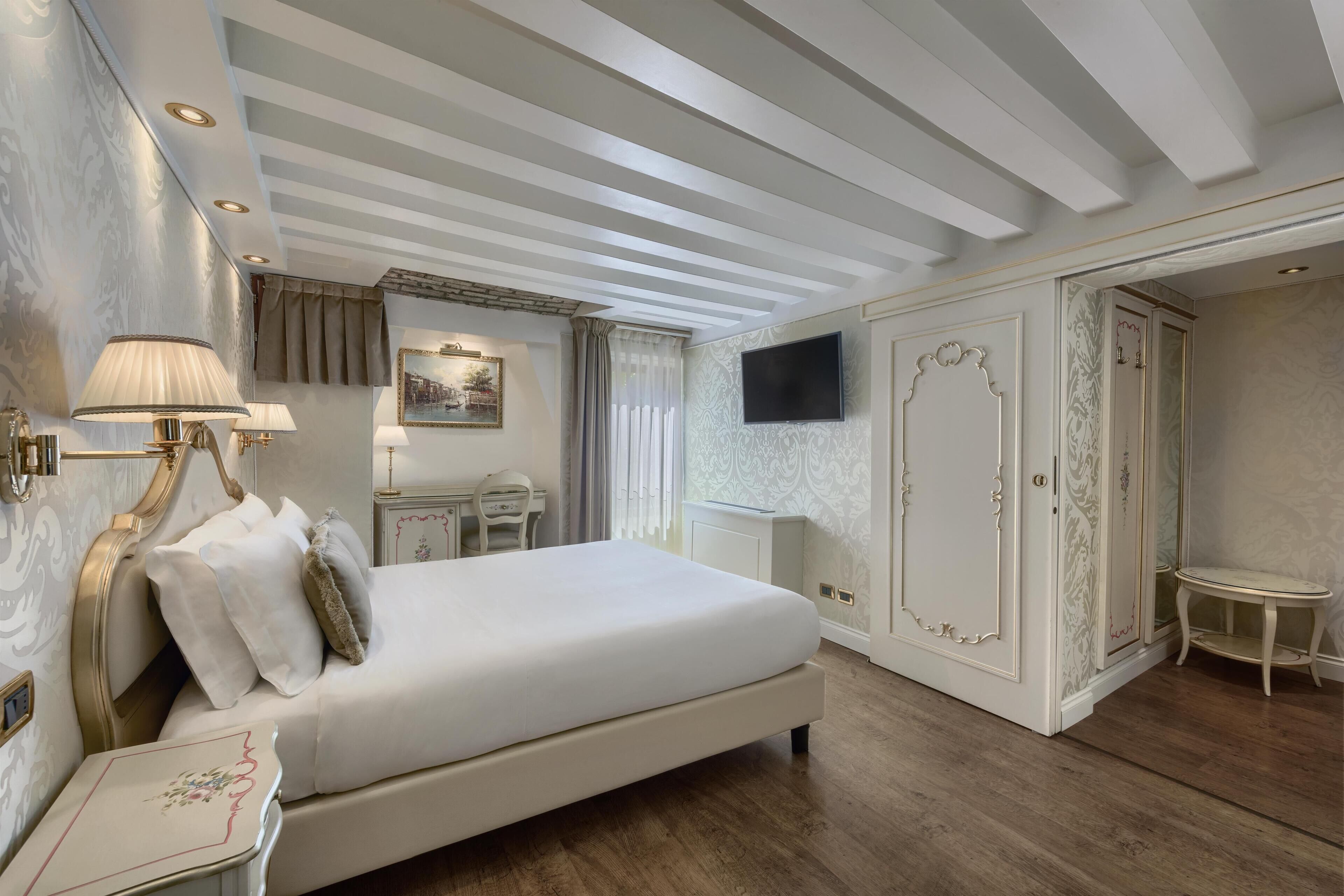 A hotel room with a large bed, a desk, a television, and a wardrobe.