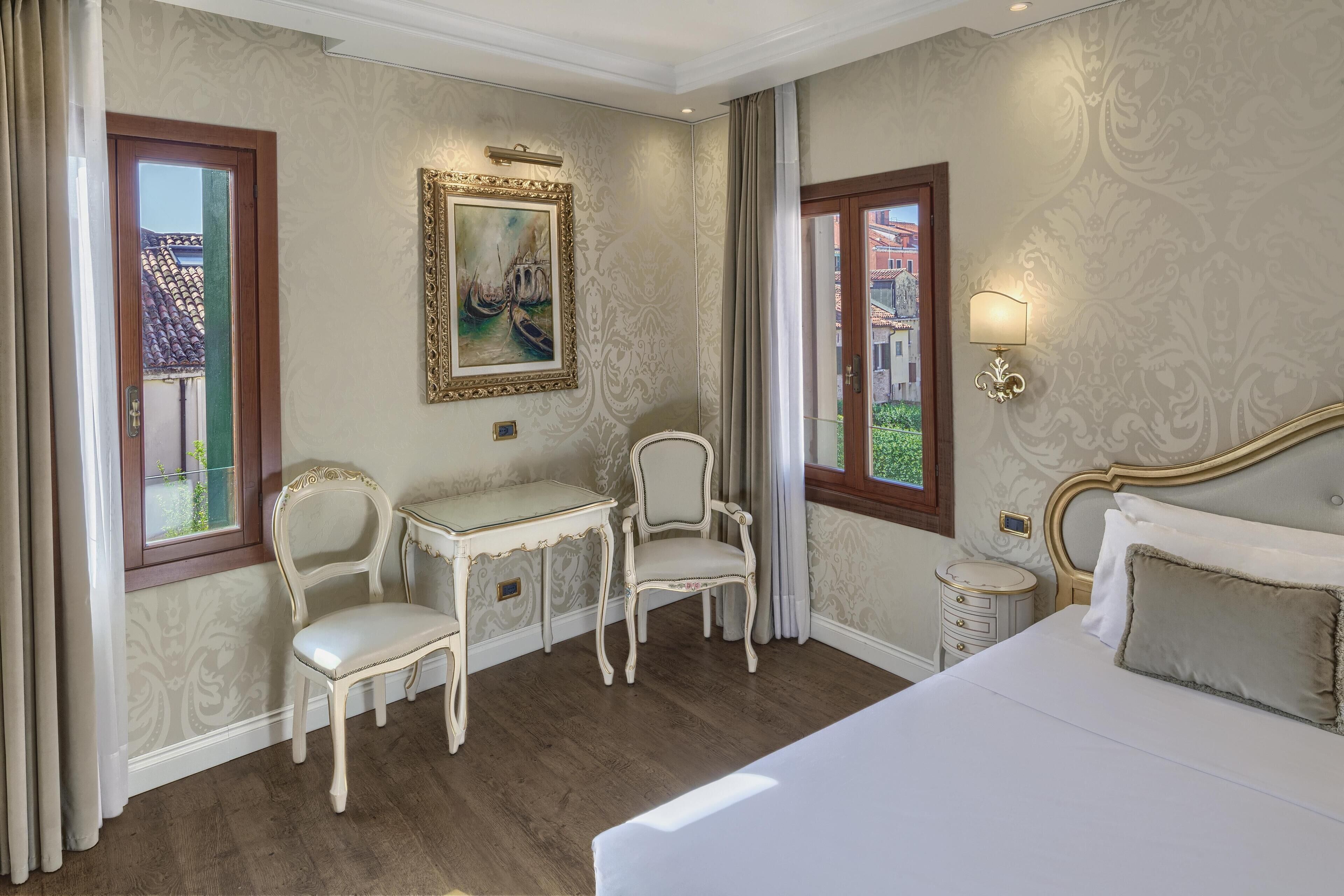A hotel room with a bed, two chairs, a small table, and a painting on the wall.