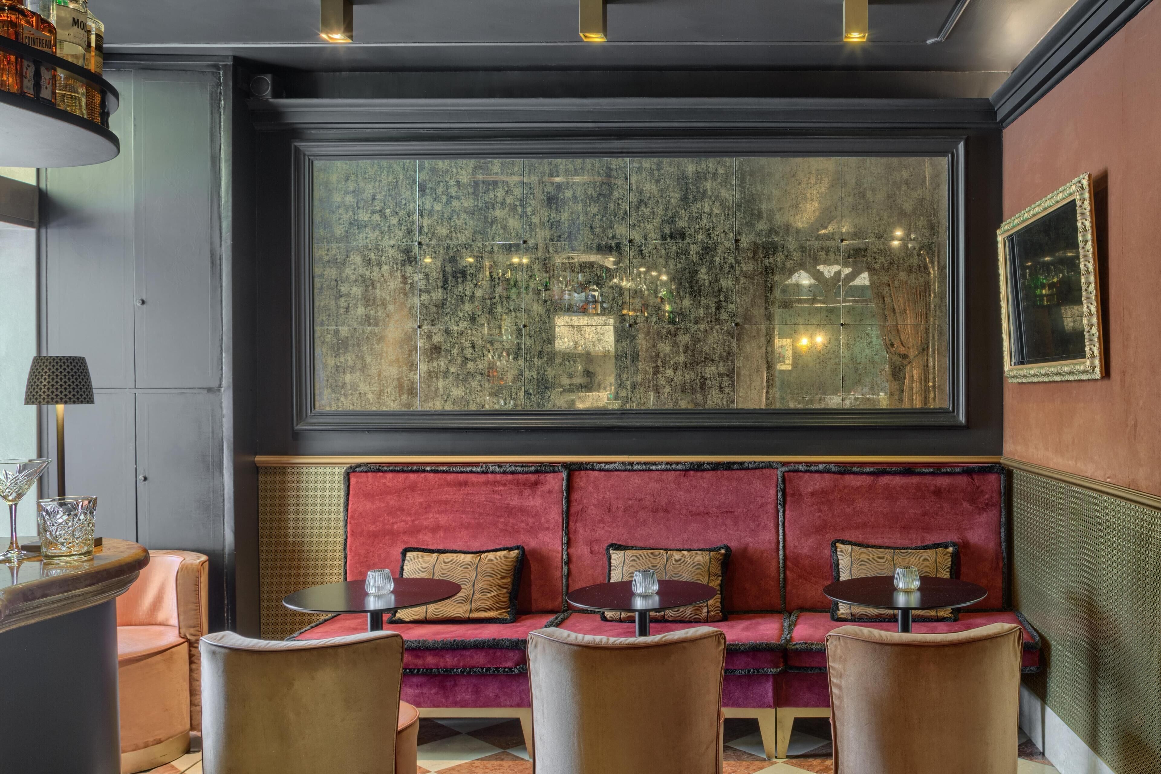 A seating area with a red velvet sofa, cushioned chairs, and a large window with a view of a cityscape.