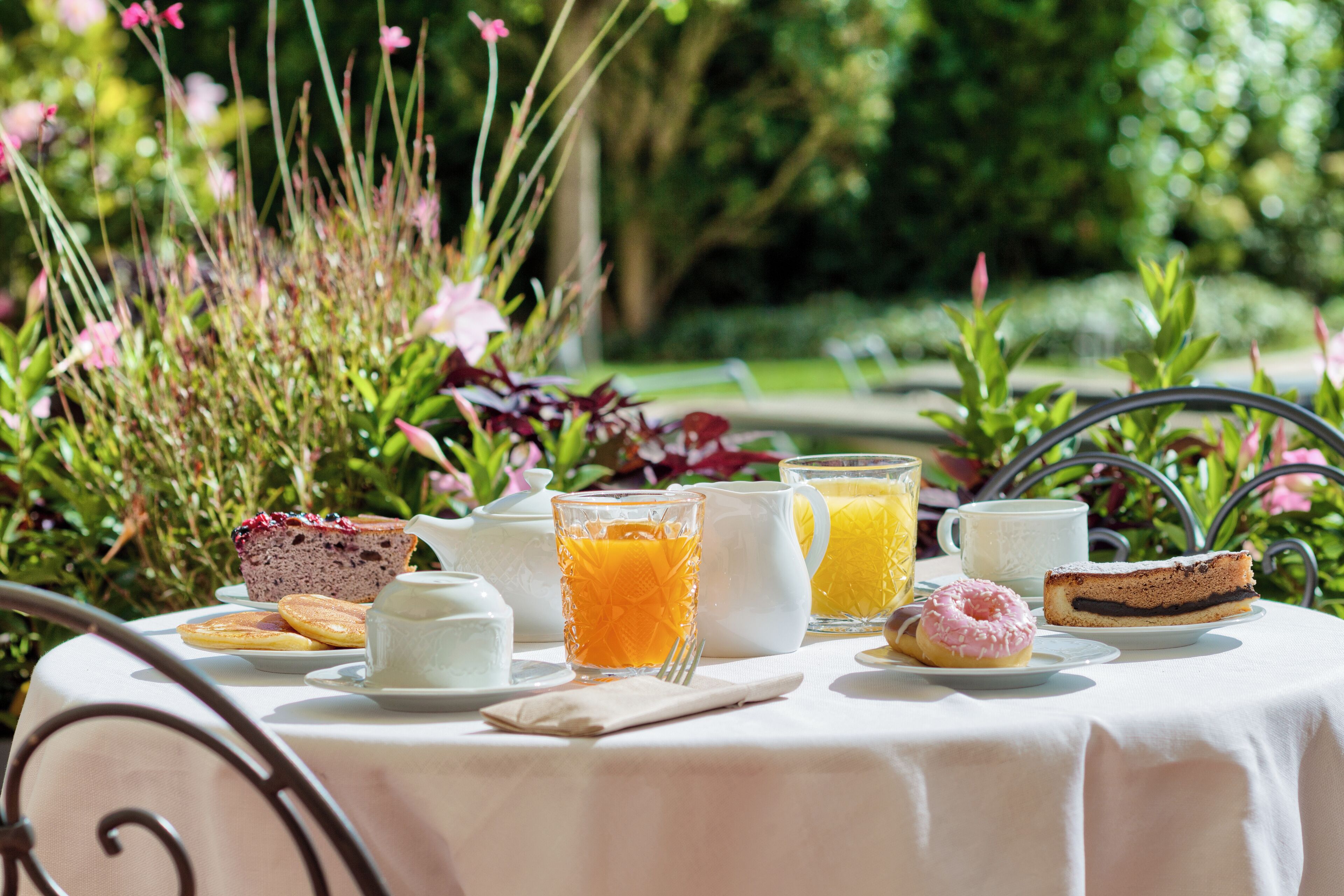 A table set outdoors with a variety of food items and drinks, surrounded by greenery.