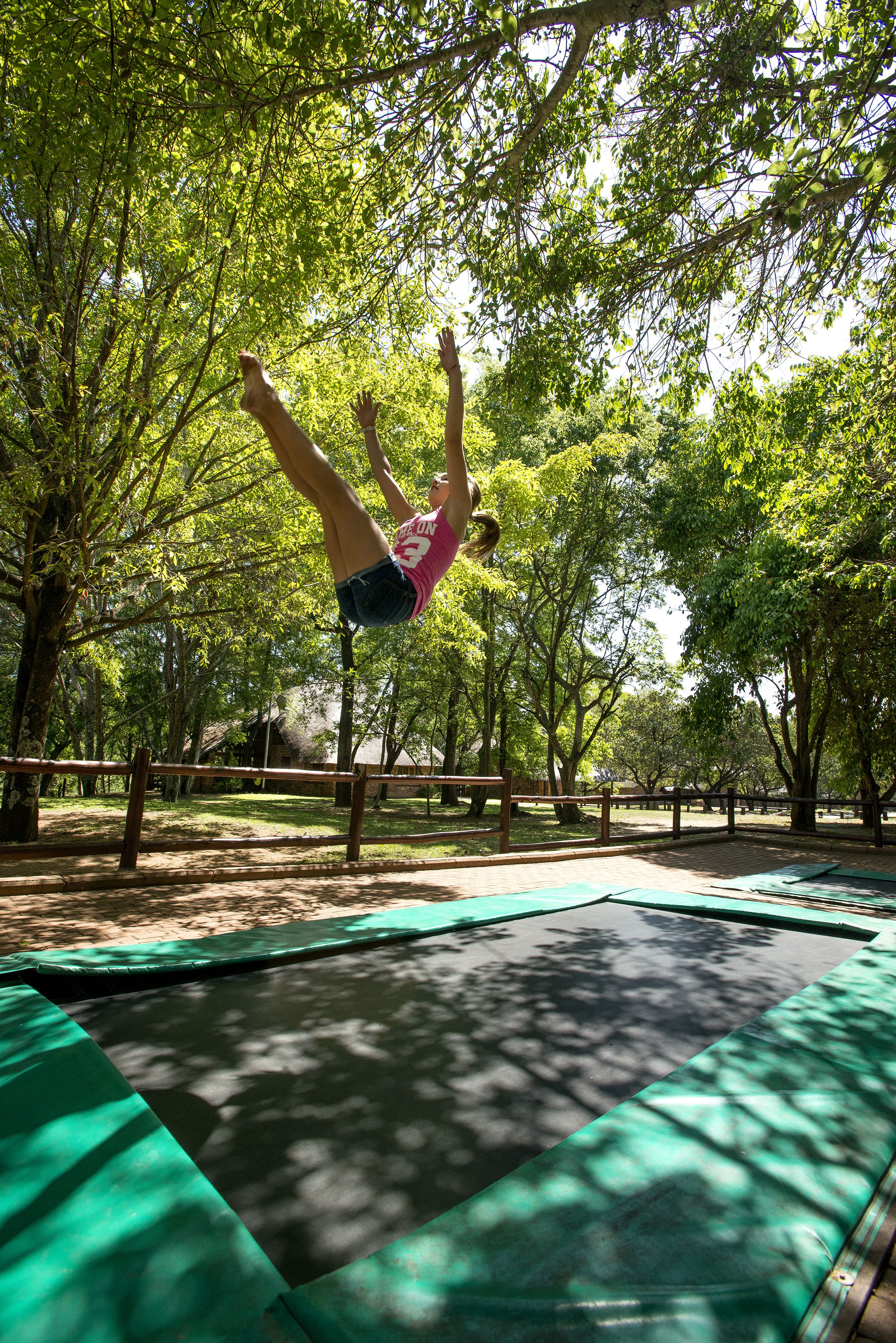 Una persona haciendo un pino en un trampolín rodeado de árboles.