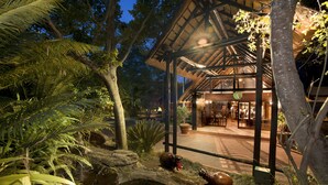 A covered outdoor area with a dining space, surrounded by tropical vegetation and a small pond. - Kruger Park Lodge (Mbombela)