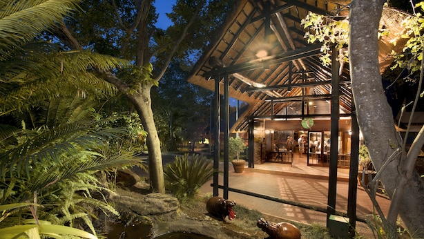 A covered outdoor area with a dining space, surrounded by tropical vegetation and a small pond. - Kruger Park Lodge (Mbombela)