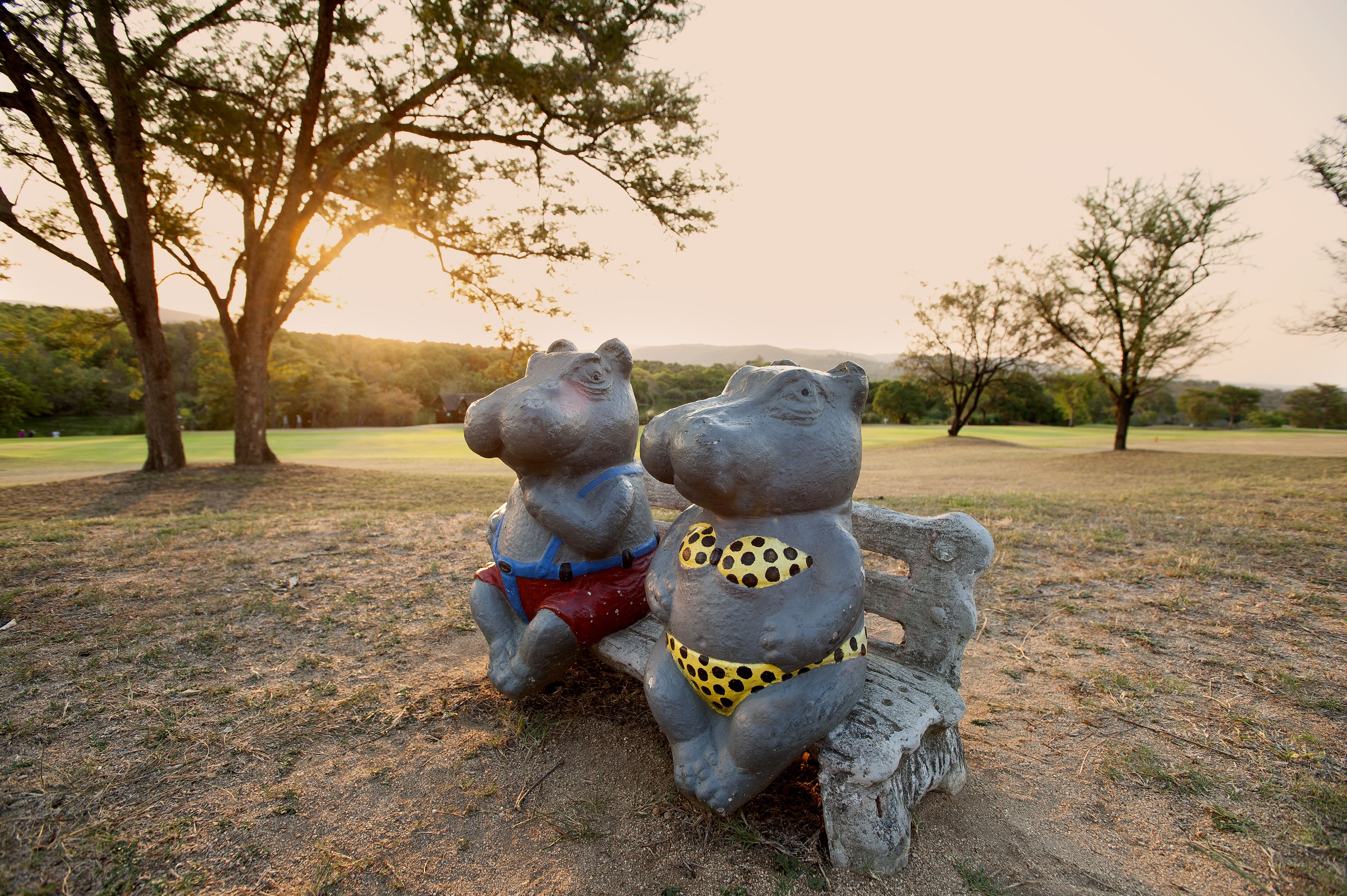 Two stone sculptures of bears sitting on a bench in a park.