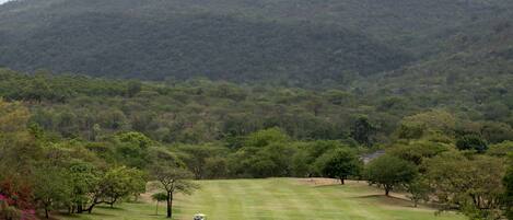 A golf course with a hilly backdrop, open grassy areas, and scattered trees.