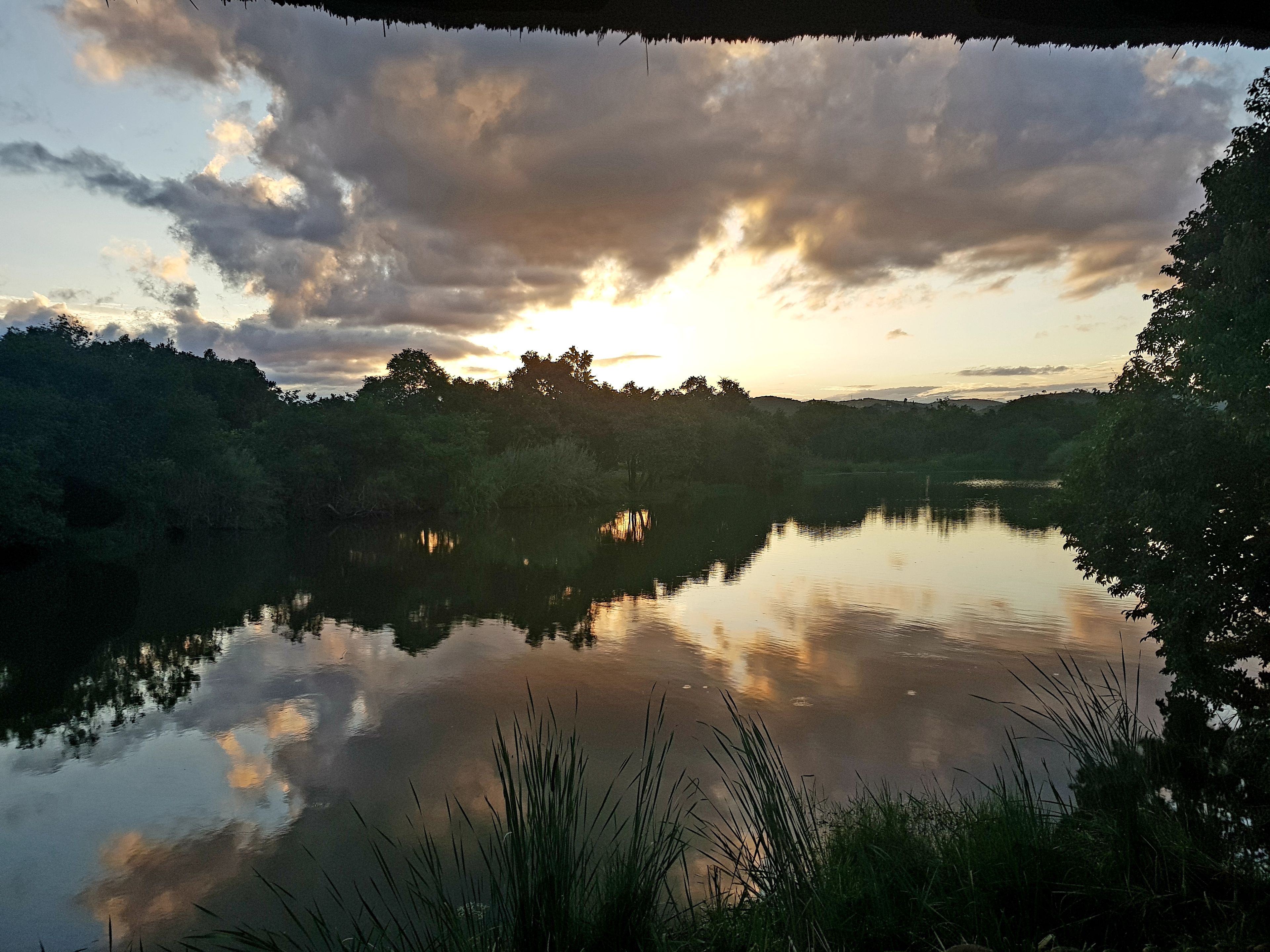 A calm lake reflecting the sky with trees and hills in the background.