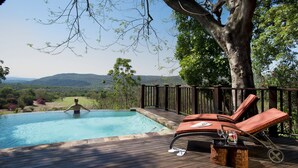 A pool area with a wooden deck, lounge chairs, and a view of the landscape. - Kruger Park Lodge (Mbombela)