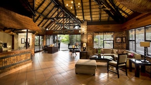 A spacious lobby with a high ceiling, a reception desk, seating area, and large windows. - Kruger Park Lodge (Mbombela)