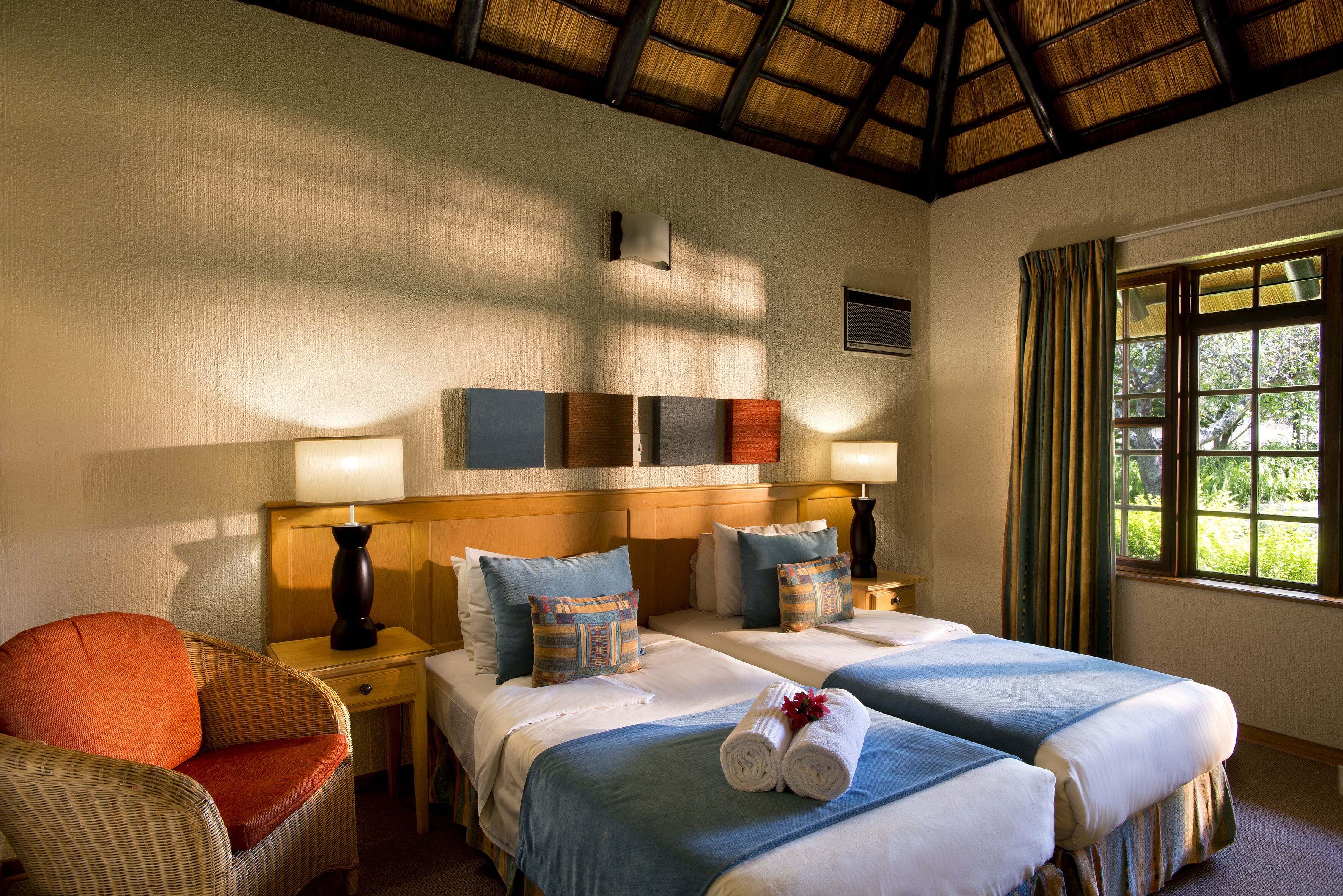 A hotel room with two beds, a nightstand, a chair, and a window with curtains.