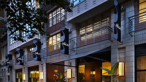 Fachada moderna de hotel con amplios ventanales, balcones y señalización iluminada.