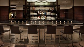 Un área de bar moderna con una barra central, varias estanterías llenas de botellas y taburetes de bar.