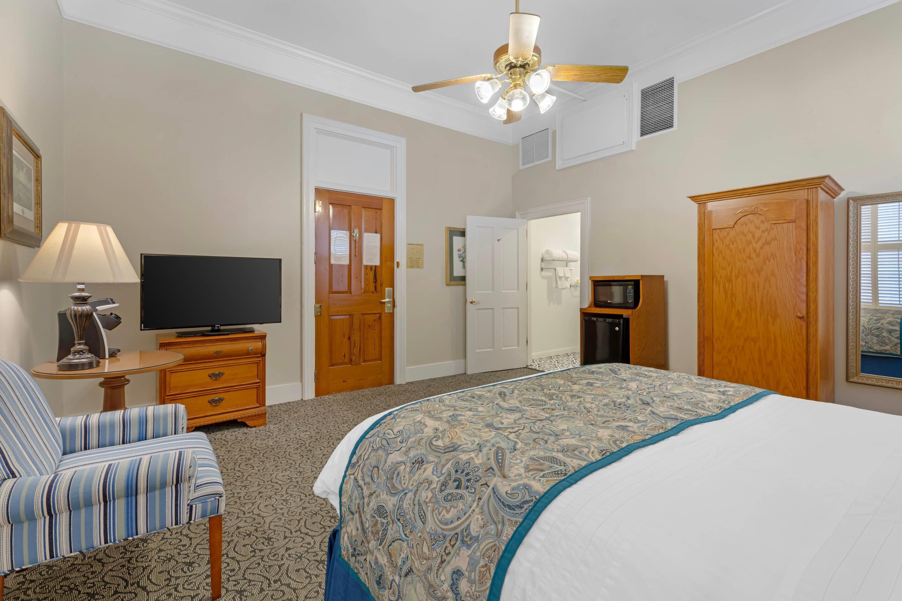 A bedroom with a bed, a television, a dresser, a chair, and a wardrobe.