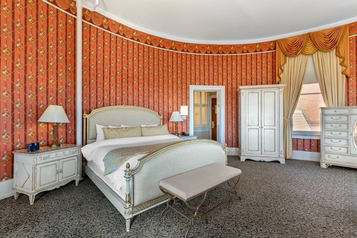 A classic room with a large bed, a bedside table, a bench, a wardrobe, and a dresser.
