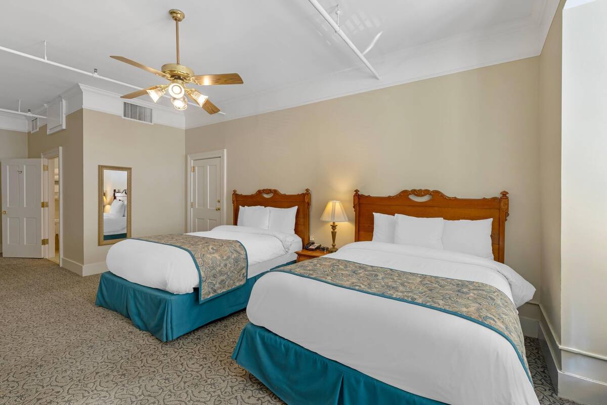 A hotel room with two beds, a ceiling fan, a mirror, and a nightstand with a lamp.