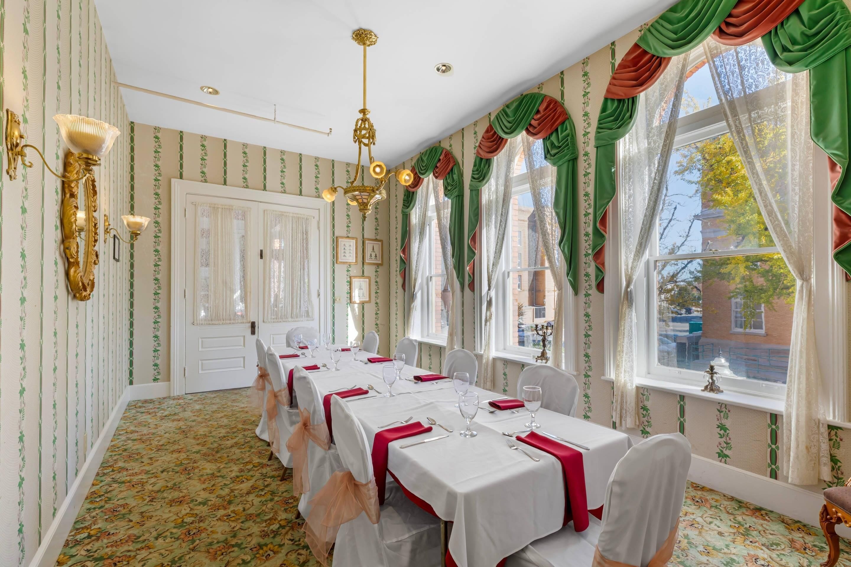 Une salle à manger avec une longue table dressée pour le repas, un lustre et un papier peint à motifs.