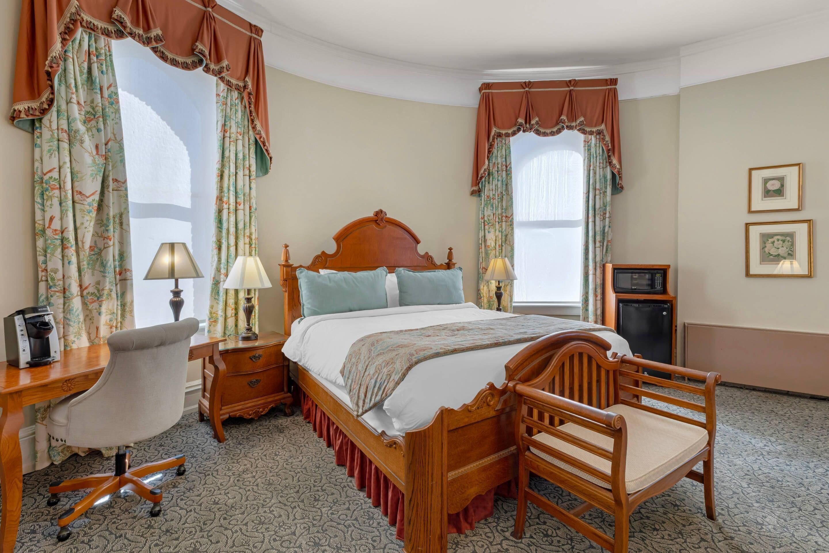 A bedroom with a wooden bed, two bedside tables with lamps, a desk with a chair, and a small cabinet.