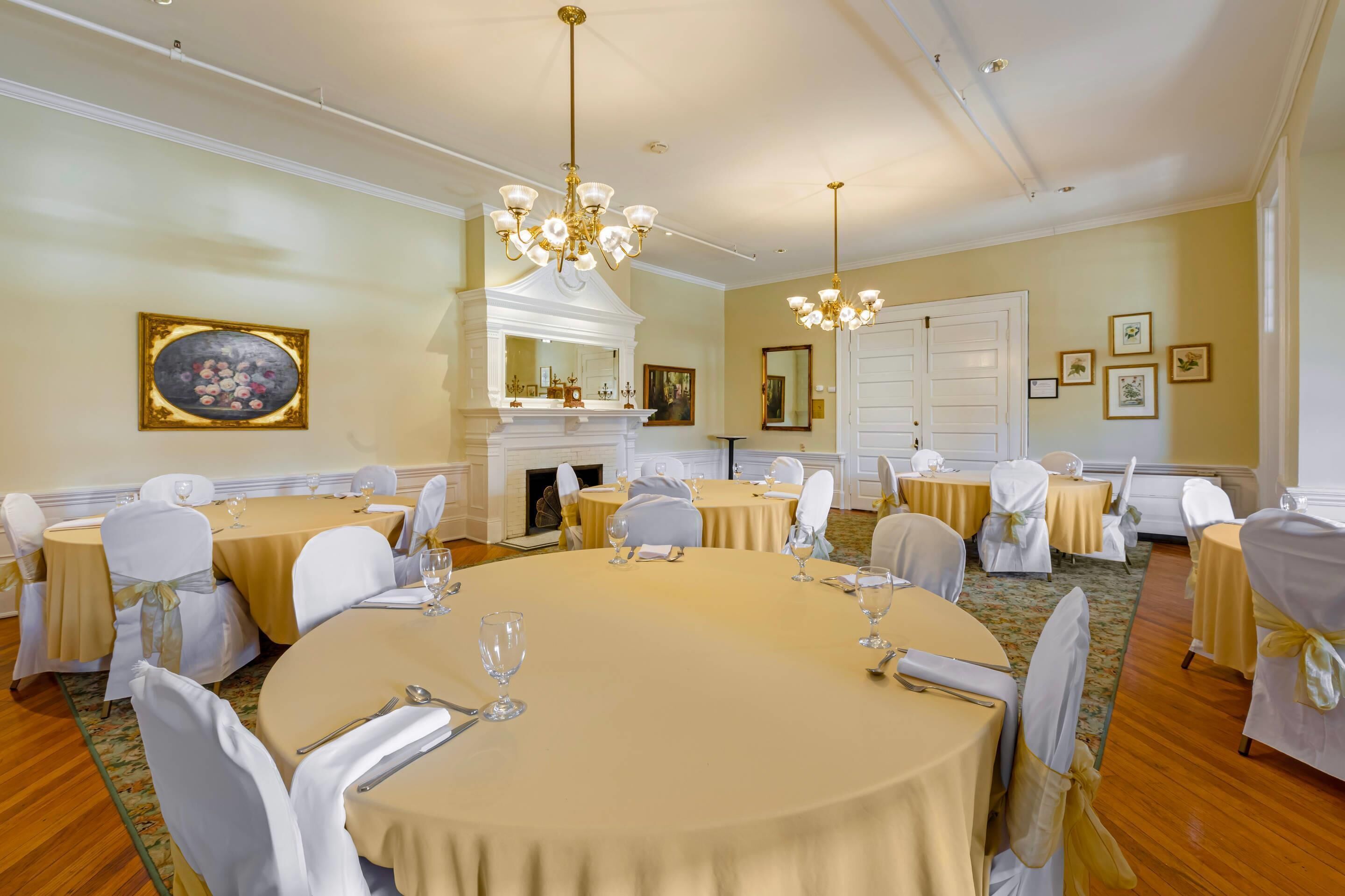 Un comedor formal con mesas redondas, sillas blancas, candelabros y cuadros en las paredes.