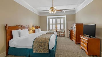 Habitación de hotel con una cama grande, televisor, escritorio con silla y ventana con persianas.