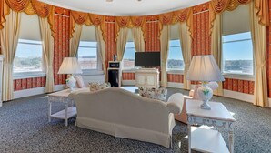 A hotel room with a large bed, two bedside tables, a ceiling fan, a TV, and a view of the outdoors. - Windsor Hotel, an Ascend Collection Hotel (Americus)