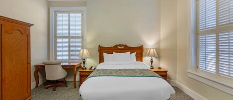 A hotel room with a large bed, a wooden wardrobe, a desk with a chair, and two bedside lamps.
