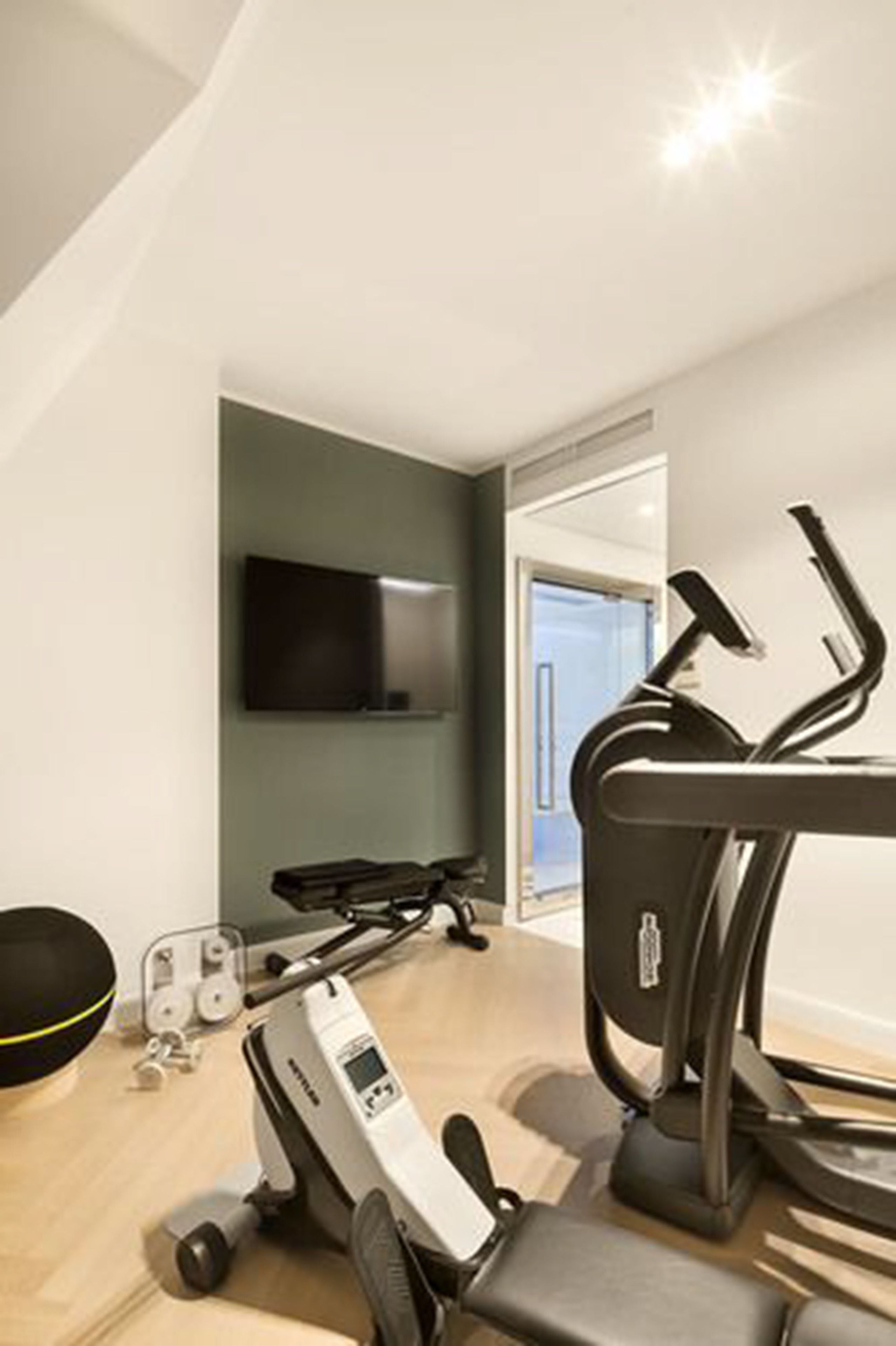 Un gimnasio moderno con equipo de ejercicio, un televisor y una puerta que da a otra habitación.