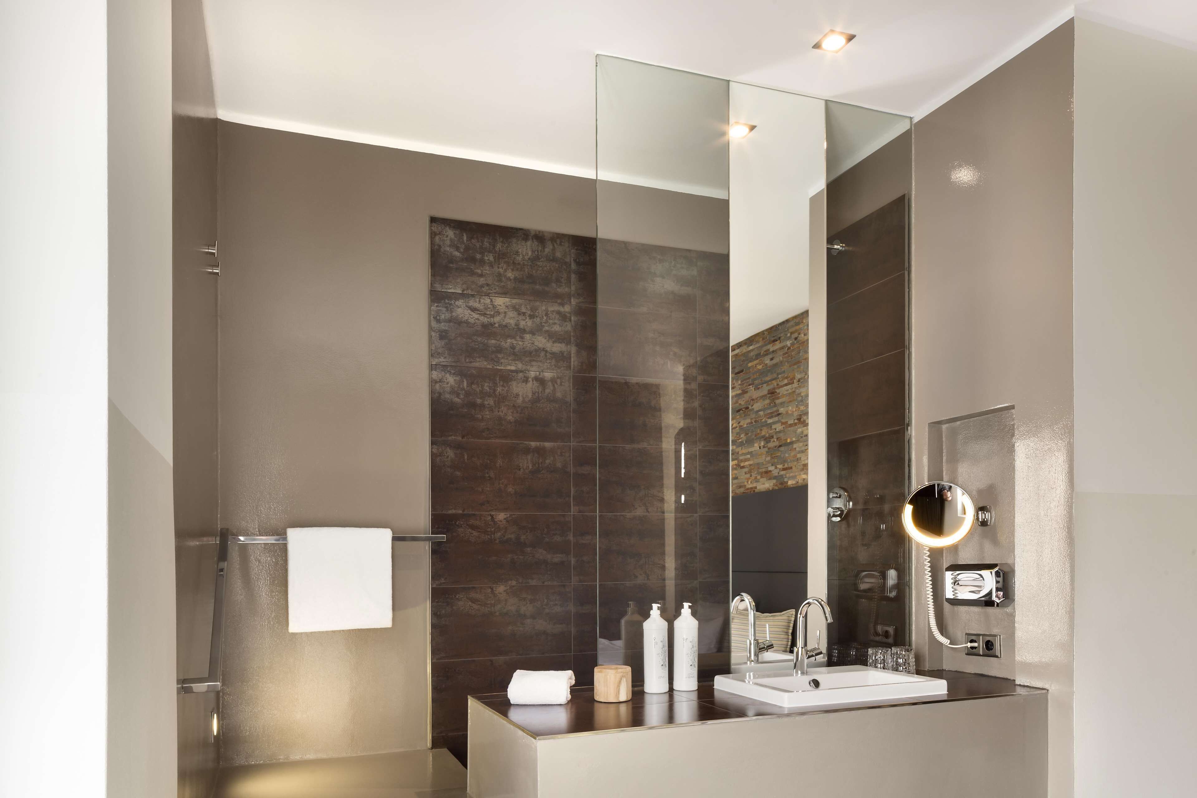 A modern bathroom with a glass shower enclosure, a large mirror, and a vanity with a sink and toiletries.