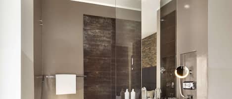 Un baño moderno con cabina de ducha de vidrio, un espejo grande y un tocador con lavabo y artículos de aseo.
