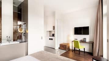 Una habitación de hotel moderna con una cama grande, una zona de estar con una silla, un escritorio, un televisor de pantalla plana y una kitchenette.