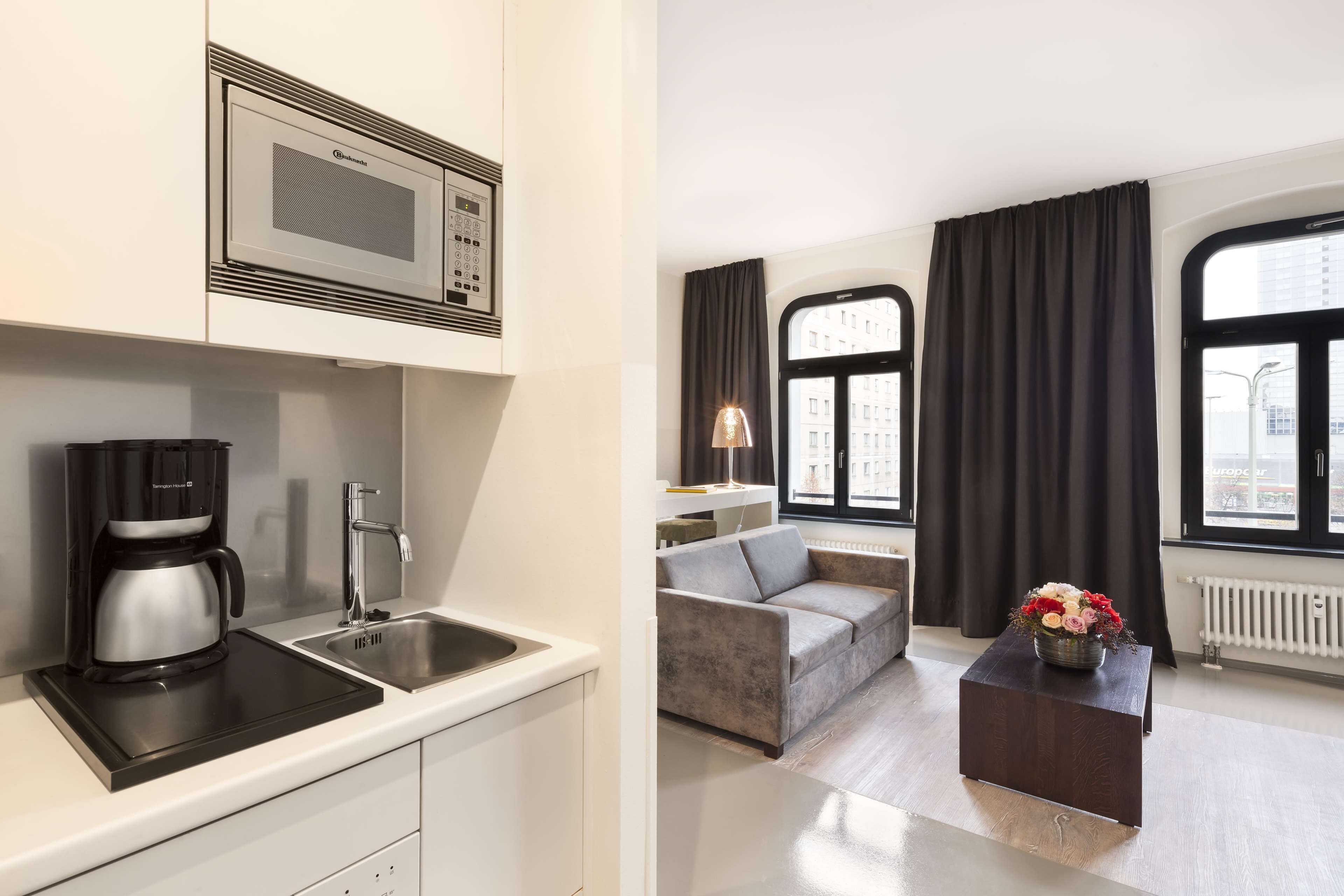 A modern kitchen with a coffee maker and a microwave, a sofa, and a window with curtains.
