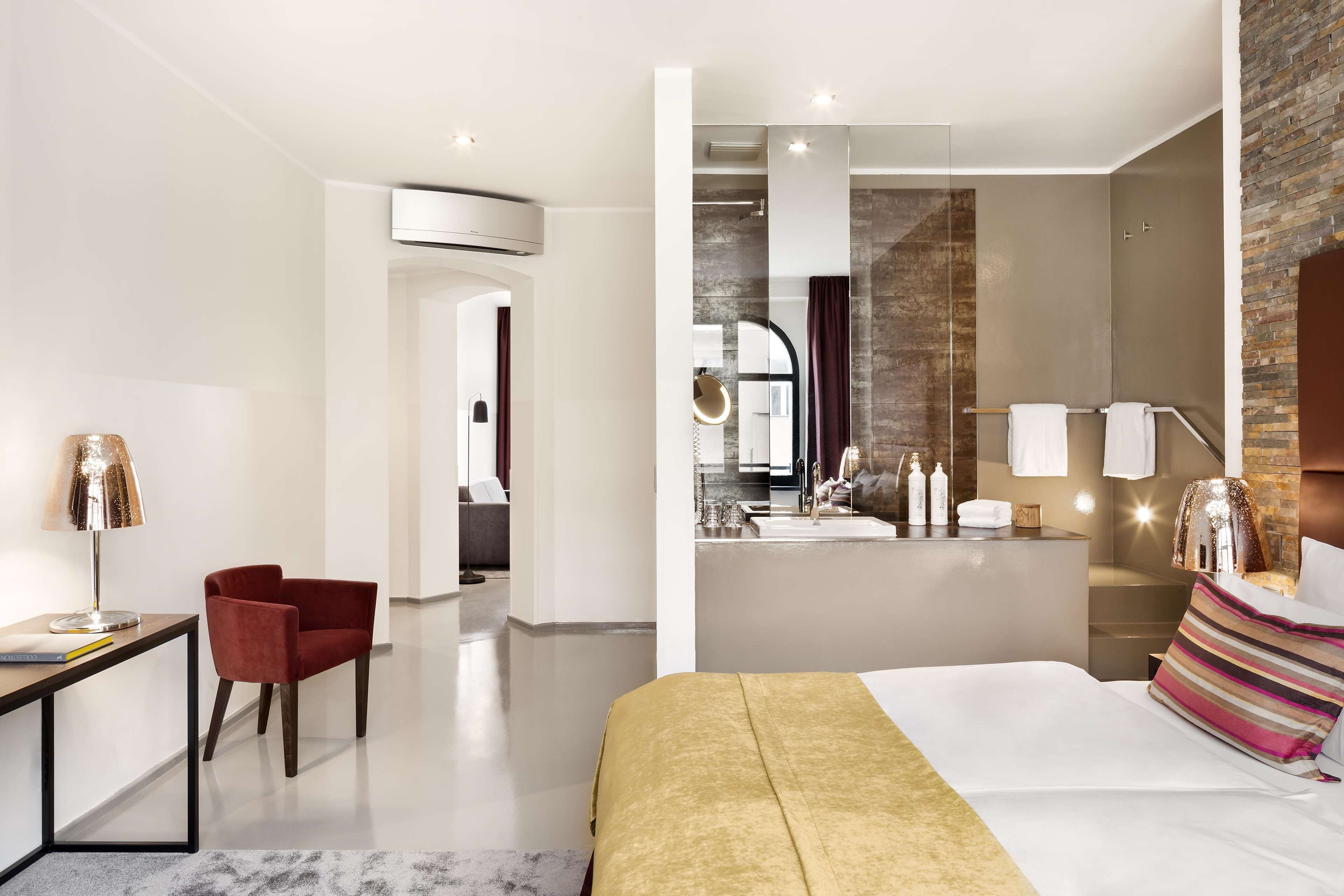 Habitació d'hotel moderna amb un llit gran, una taula de treball amb una cadira, un tocador amb mirall i un bany amb dutxa i vàter.