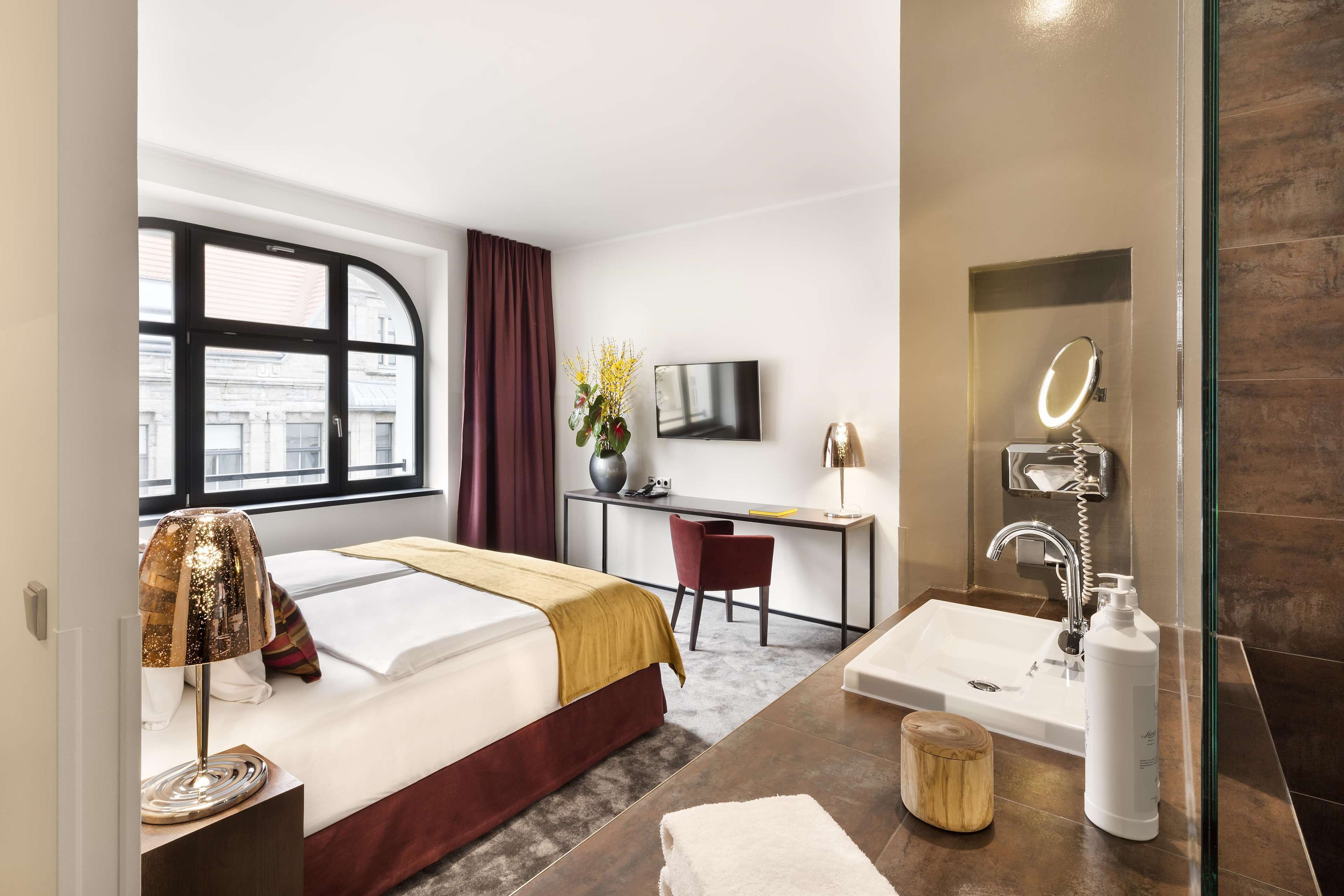 Ein Hotelzimmer mit Bett, Schreibtisch, Stuhl, Fernseher und einem Badezimmer mit Waschbecken und Spiegel.