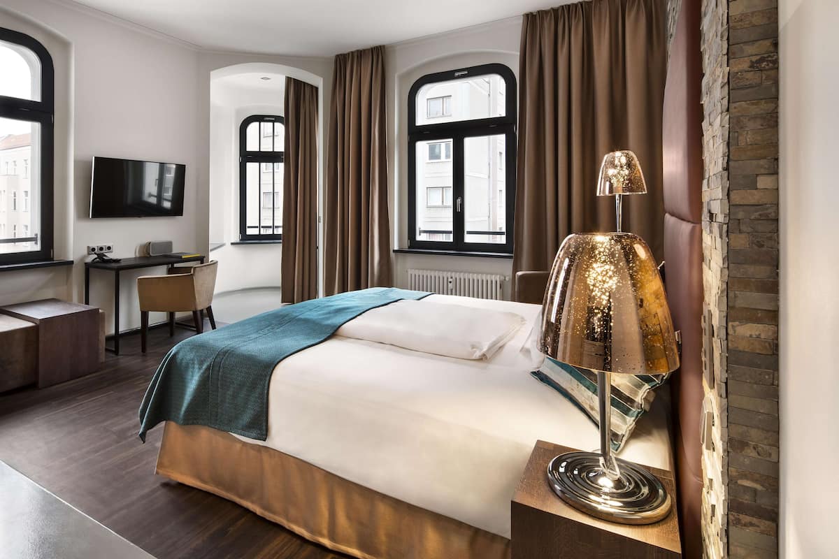 Una camera d'albergo moderna con un letto grande, una scrivania, una TV e una lampada.