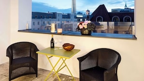 A balcony with two wicker chairs, a small table, and a vase of flowers. A bottle and glasses are on the table. The view includes a tower and buildings. - Lux 11 Berlin Mitte (Berlin)