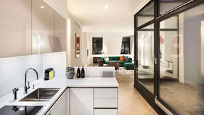 A modern kitchen with a central island, stainless steel appliances, and a view into a living area with a green sofa and cityscape. - Lux 11 Berlin Mitte (Berlin)