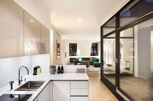 A modern kitchen with a central island, stainless steel appliances, and a view into a living area with a green sofa and cityscape.