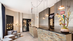A modern reception area with a stone-textured counter, grey seating, and a decorative floral arrangement. - Lux 11 Berlin Mitte (Berlin)