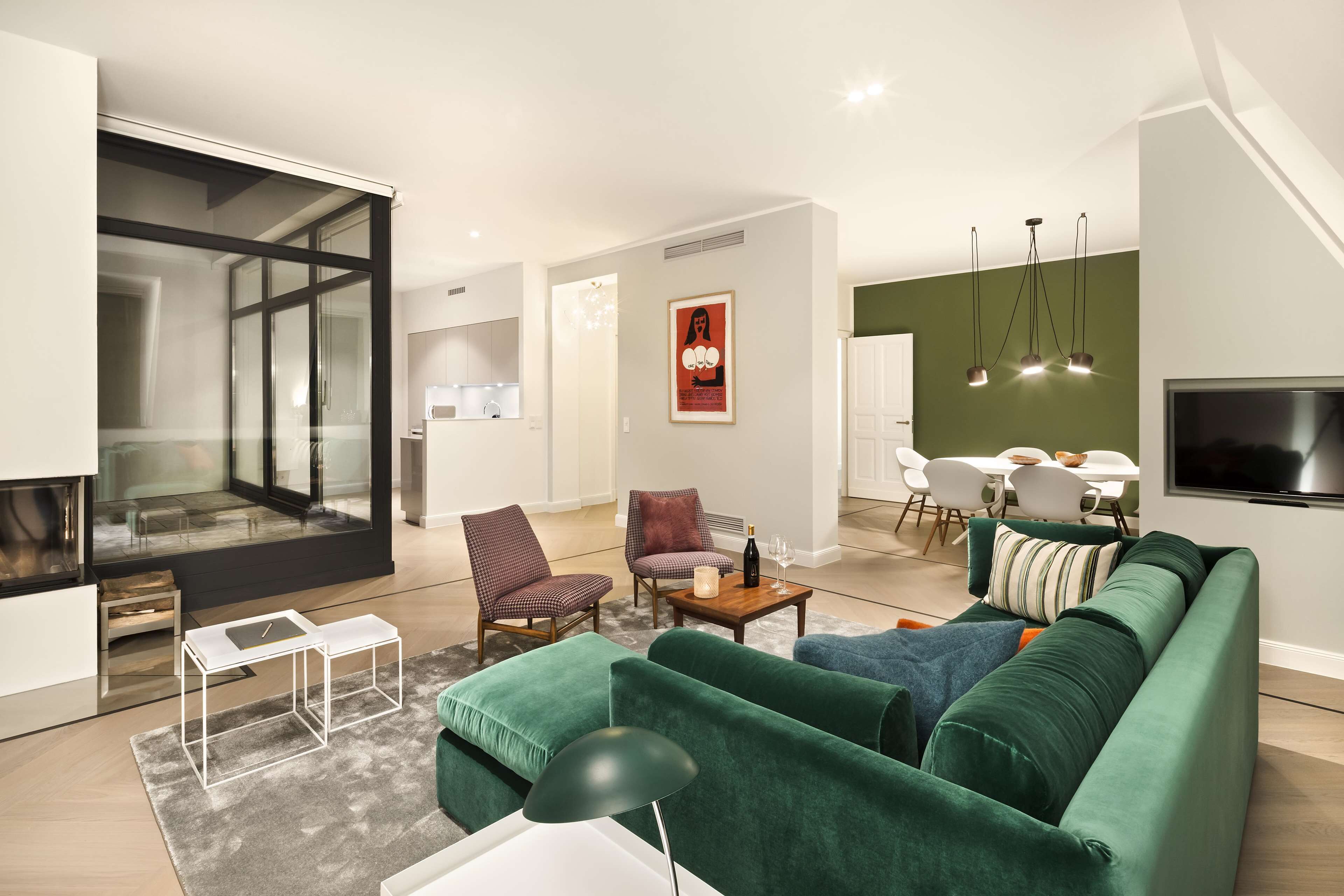 A modern living room with a green sofa, a coffee table, and a TV. There is a dining area with a table and chairs.