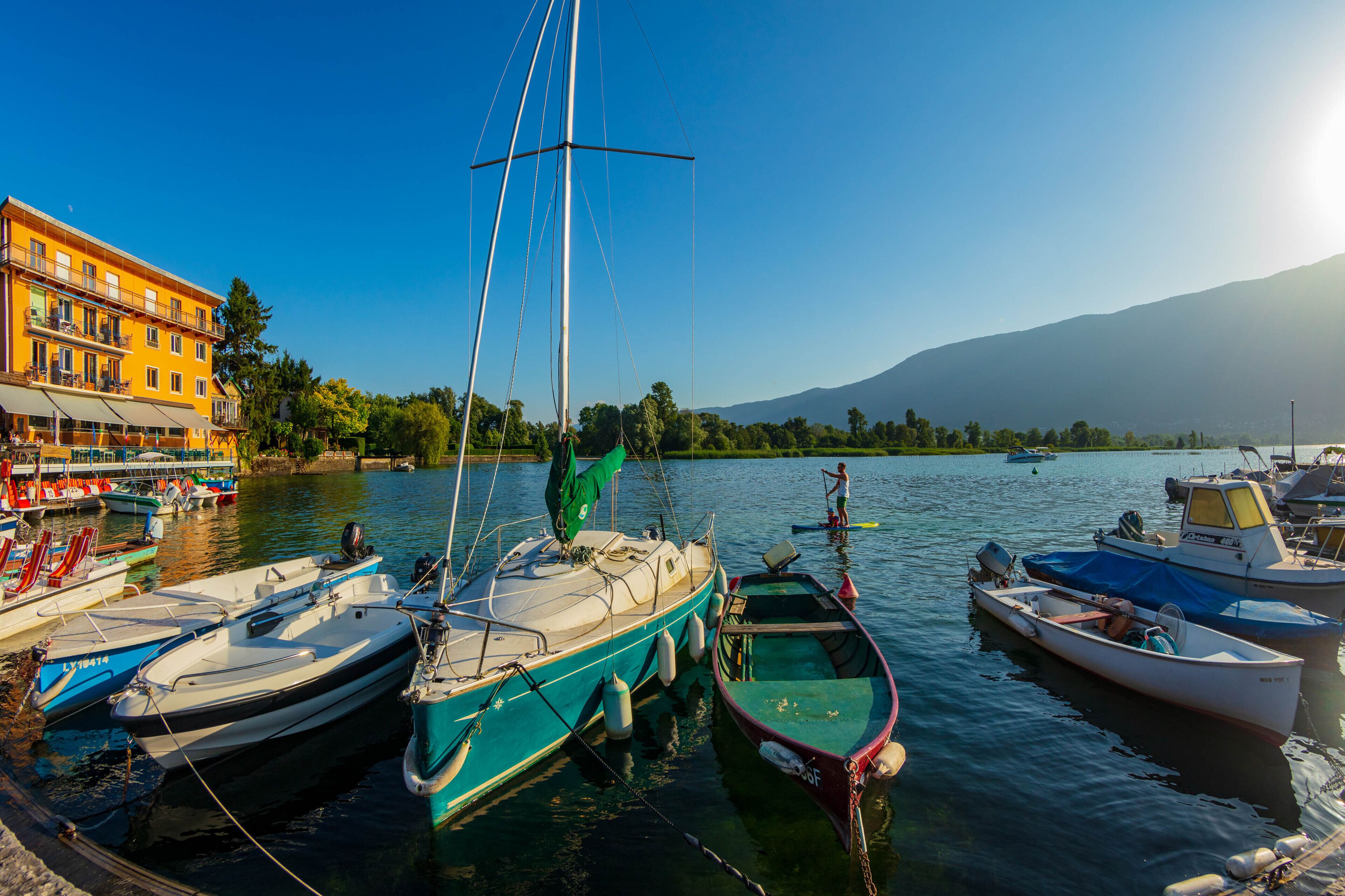 Uma marina com vários barcos atracados, um edifício com varandas e uma montanha ao fundo.