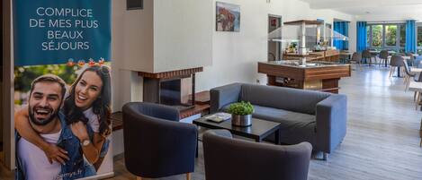 A modern hotel lobby with a fireplace, comfortable seating, and a dining area.