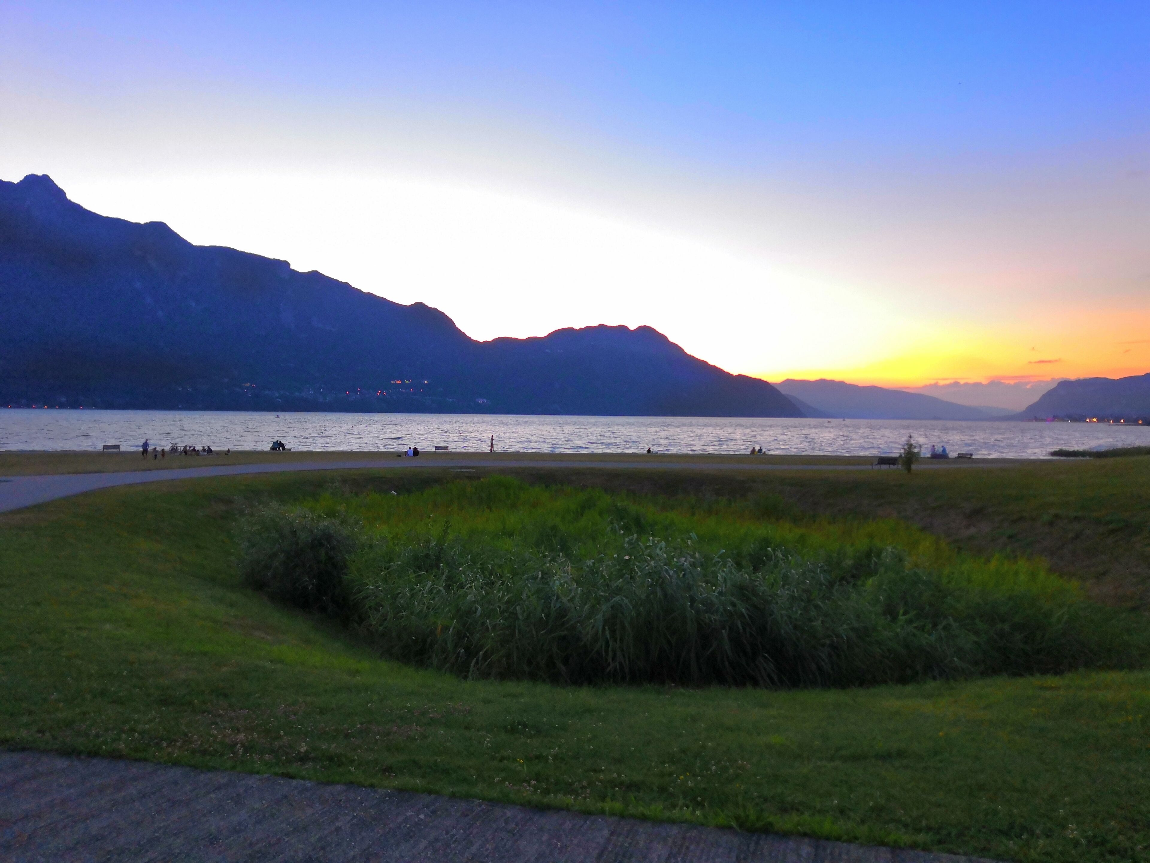A lakeside view with mountains in the background and a grassy foreground.