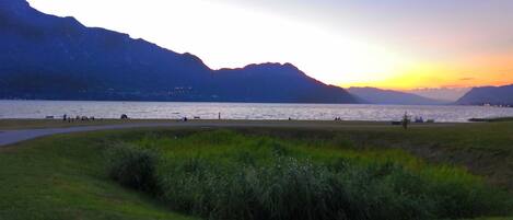 A lakeside view with mountains in the background and a grassy foreground.