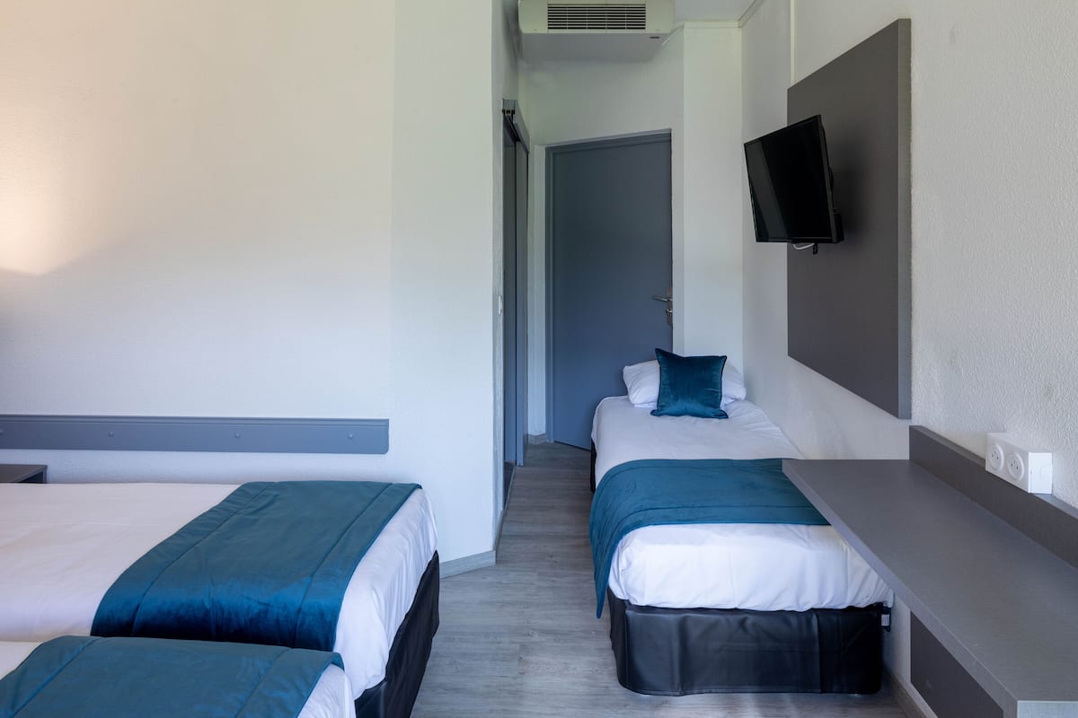 A hotel room with two beds, a TV mounted on the wall, and a door leading to another room.